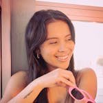 Bright photo of a young woman in Buenos Aires holding pink sunglasses indoors.